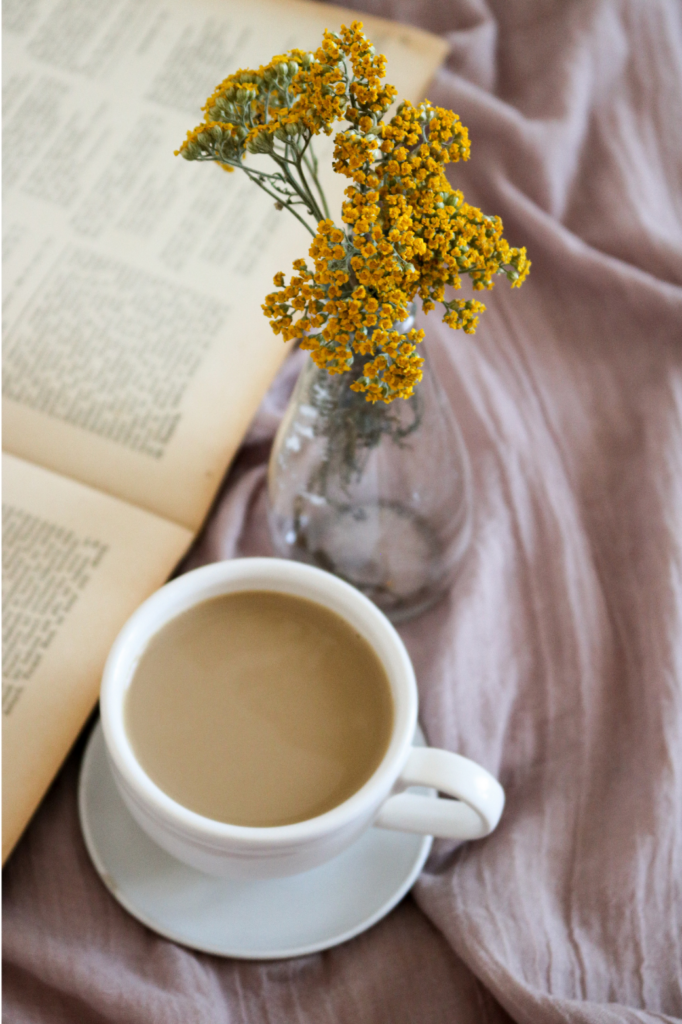 coffee cup sits next to an open book with yellow flowers